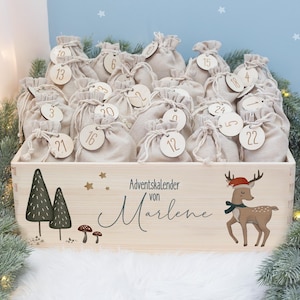 Könnte beinhalten: Ein Adventskalender aus Holz, gefüllt mit kleinen beigefarbenen Stoffbeuteln, jeweils mit einem Holzanhänger mit der Nummer 1-24. Die Box ist mit einem Hirsch mit Weihnachtsmütze, Bäumen und dem Text "Adventskalender von Marlene" verziert.