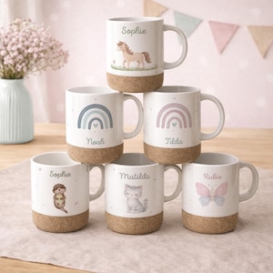 Könnte beinhalten: Weiße Keramikbecher mit Korkböden, mit verschiedenen Illustrationen und Namen. Designs umfassen ein Pferd, Regenbogen, eine Katze, einen Otter und einen Schmetterling. Namen auf den Bechern sind Sophie, Noah, Tilda, Matilda und Rubie.