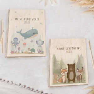 Op de afbeelding: Twee houten opbergdozen voor kunstwerken met illustraties. De eerste doos heeft een blauwe walvis, een octopus en andere zeedieren. De tweede doos heeft een beer, een vos, een hert en een konijn in een boslandschap. Beide dozen hebben de tekst "Meine Kunstwerke Arthur".
