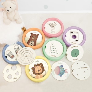 Puede incluir: Colección de juguetes de madera coloridos con varios diseños. Los juguetes incluyen ilustraciones de un oso, un león y un pez, junto con otros patrones y texto. Los juguetes son redondos con un marco de madera.