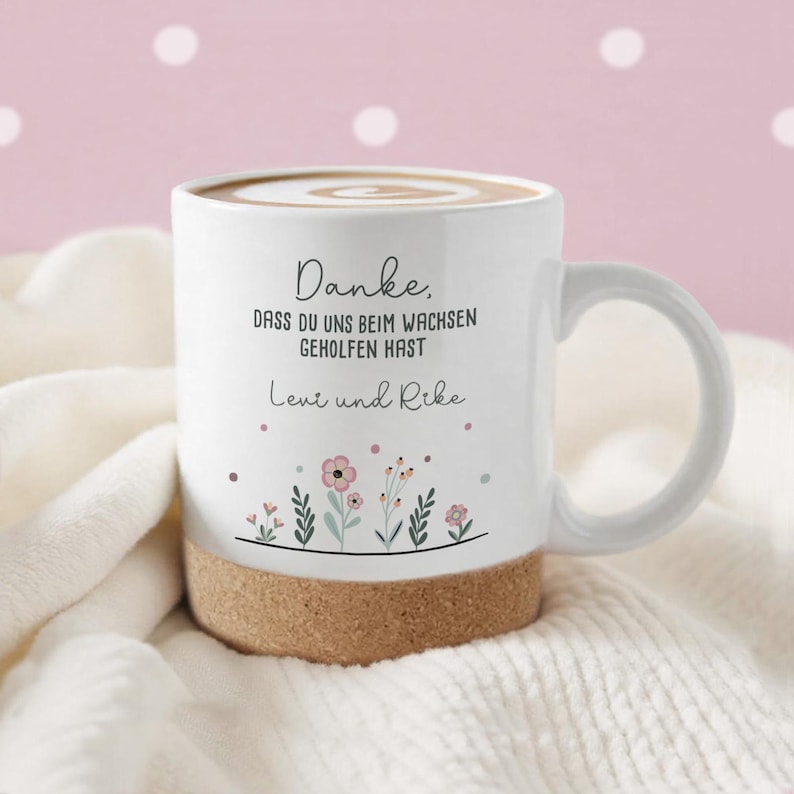 May include: White ceramic mug with a cork base, filled with a beverage and topped with a swirl design. The mug features the text "Danke, dass du uns beim wachsen geholfen hast" and the names "Leni und Rike" with floral illustrations.