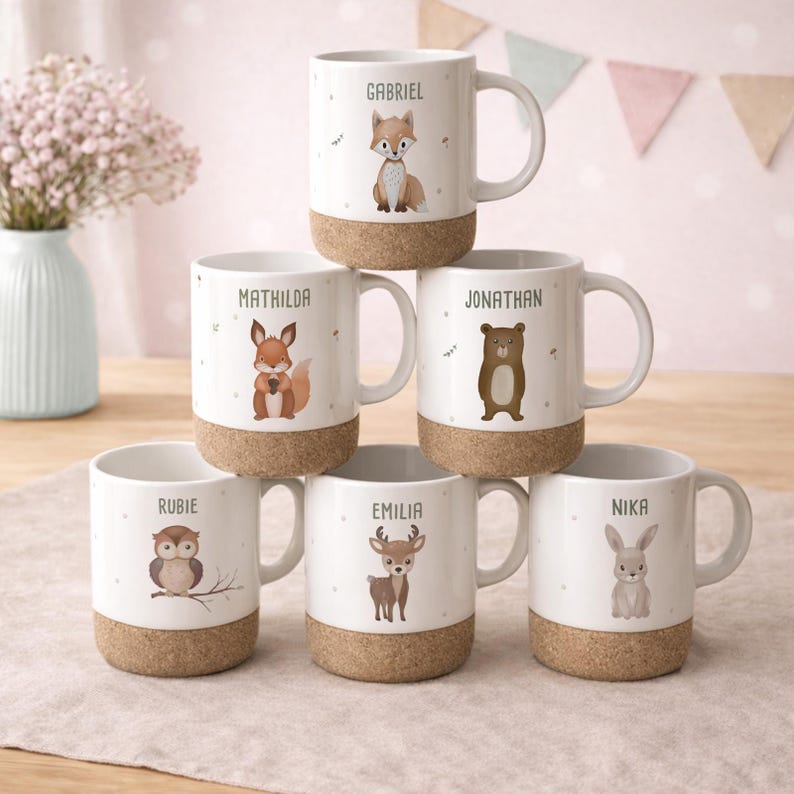 May include: White ceramic mugs with cork bases, each featuring a different woodland animal illustration and a name. The animals include a fox, bear, owl, deer, and rabbit. The names are: Gabriel, Mathilda, Jonathan, Rubie, Emilia, and Nika.
