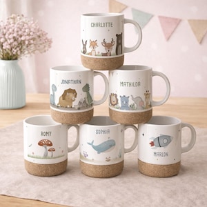 Könnte beinhalten: Weiße Keramikbecher mit Korkböden, jeweils mit einem Namen und einer einzigartigen Illustration. Zu den Namen gehören Charlotte, Jonathan und Sophia, mit Designs wie einer Rakete, einem Wal und Waldtieren. Die Becher sind gestapelt.