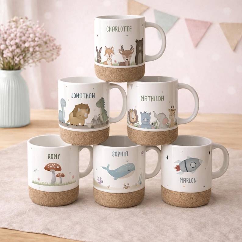 May include: White ceramic mugs with cork bases, each featuring a different name and a unique animal or object illustration. The mugs include names like Charlotte, Jonathan, and Sophia, with designs such as a rocket, whale, and forest animals.