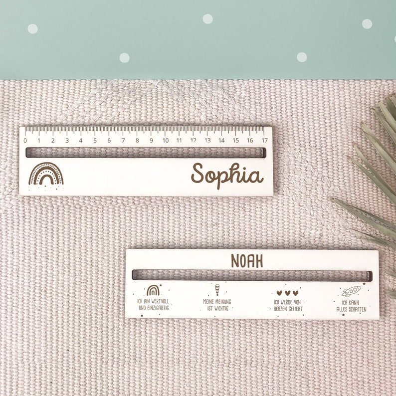 May include: Two white wooden rulers with a rainbow design and personalized names. The top ruler says "Sophia" and the bottom ruler says "Noah". The bottom ruler also has four phrases: "I am valuable and unique", "My opinion is important", "I am loved from the heart", and "I can achieve anything".