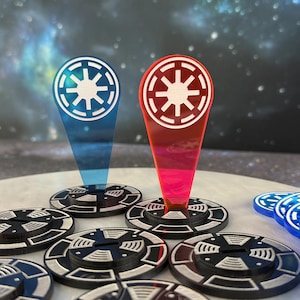 Peut inclure: Un ensemble de jetons de jeu circulaires noirs et blancs arborant un emblème en forme d'étoile. Deux marqueurs en acrylique translucide, l'un bleu et l'autre rouge, sont dressés, chacun affichant une étoile blanche dans un cercle sur un pied.