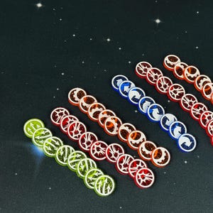 以下が含まれることがあります： 白いシンボルが付いた、10種類の異なる色のプラスチック製ゲームトークンのセット。トークンは、赤、オレンジ、黄色、緑、青の色で、行に並べて配置されています。