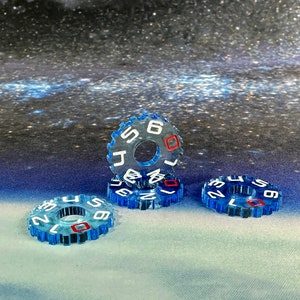 Könnte beinhalten: Drei blaue Nummernscheiben aus Kunststoff mit weißen Zahlen und roten Akzenten. Die Scheiben sind übereinander gestapelt.