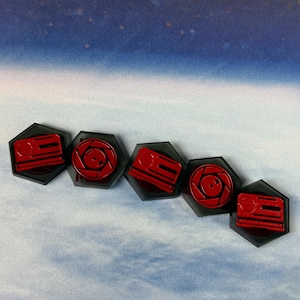 May include: Five red and black hexagonal game pieces. Each piece has a red design on a black background. The designs include a series of lines and a circular design. The pieces are arranged in a row.