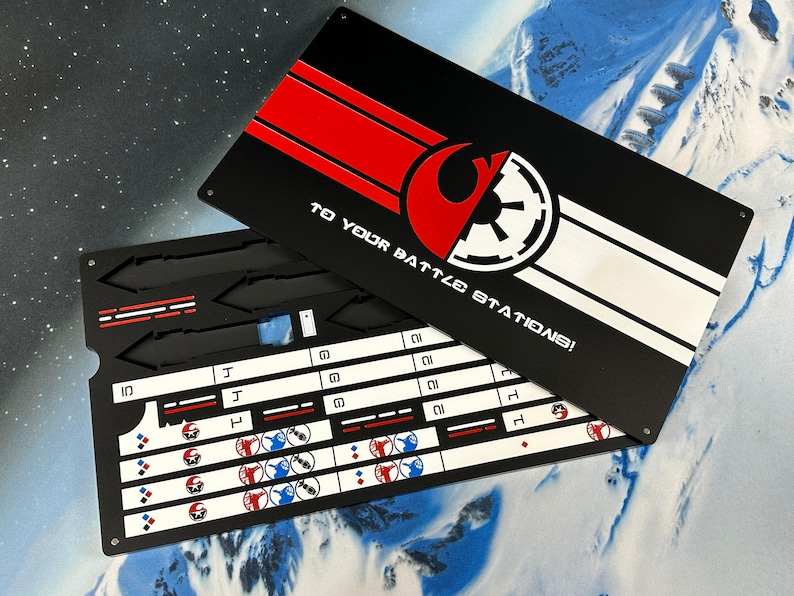 May include: A rectangular black metal game board with a lid featuring a red and white graphic design, the text "TO YOUR BATTLE STATIONS!", and symbols of two opposing factions. The base contains recessed slots and white printed grids with icons.