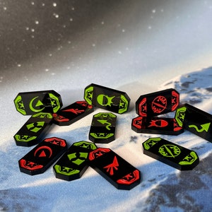 May include: A set of 12 black, green, and red game tokens with various symbols. The tokens are shaped like elongated hexagons and have a glossy finish.
