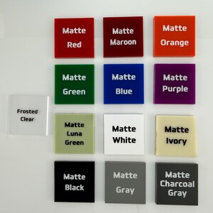 May include: A collection of thirteen square acrylic swatches arranged in a grid. Each swatch features printed text identifying its color, including Matte Red, Maroon, Orange, Green, Blue, Purple, Luna Green, White, Ivory, Black, Gray, Charcoal Gray, and Frosted Clear.