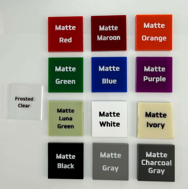 May include: A collection of thirteen square acrylic swatches arranged in a grid. Each swatch features printed text identifying its color, including Matte Red, Maroon, Orange, Green, Blue, Purple, Luna Green, White, Ivory, Black, Gray, Charcoal Gray, and Frosted Clear.