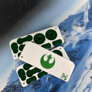 May include: A white plastic storage case with green compartments and a white lid with a green Rebel Alliance symbol. The case is open and the lid is laying on top of the case.