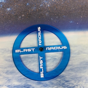 May include: A blue plastic template with the words "BLAST" and "RADIUS" printed on it. The template is used for measuring the blast radius of explosions in tabletop games.