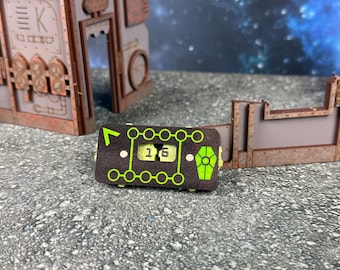 May include: A black and green game counter with the number 16 displayed. The counter has a series of green circles and lines, with a green coffin shape on one end. The background includes rusty metal structures.
