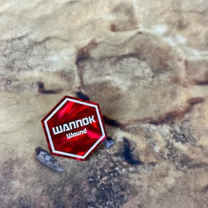 May include: A red hexagonal pin with white text that reads "ШАППОК Wound".