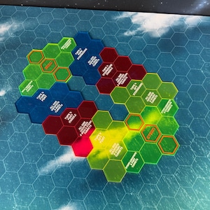 以下が含まれることがあります： 緑、青、赤、黄色の色合いの、カラフルな六角形のゲームタイル。 タイルは青と白の背景に円形に配置され、各タイルにテキストが記載されています。 ゲームは宇宙をテーマにしているようです。