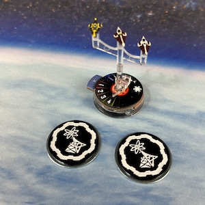 Peut inclure: Trois vaisseaux spatiaux miniatures sur un support en plastique transparent avec une base de cadran noir et rouge. Deux jetons noir et blanc avec un symbole atomique blanc et un triangle blanc avec des lignes sur un fond noir.