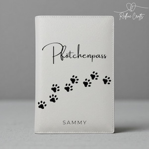 Könnte beinhalten: Ein weißer Reisepasshalter mit dem Text "Pfötchenpass" in Schreibschrift und einer Spur schwarzer Pfotenabdrücke. Der Name "SAMMY" ist unten aufgedruckt. Das Redline Crafts-Logo befindet sich in der oberen rechten Ecke.