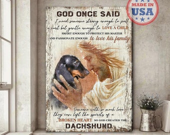 May include: A wood sign with a painting of Jesus holding a dachshund. The sign reads "God once said I need someone strong enough to pull a cart but gentle enough to love a child, smart enough to protect his master and passionate enough to love his family. Someone with so much love they can lift the spirits of a broken heart so God created the dachshund."