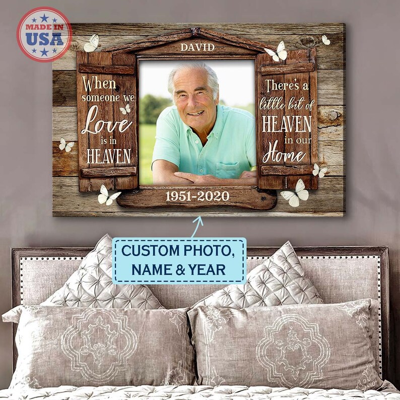 May include: A wooden memorial canvas with a photo of a man in a light blue shirt. The canvas has a window design with the text "When someone we love is in HEAVEN" on the left and "There's a little bit of HEAVEN in our Home" on the right. The text "DAVID 1951-2020" is below the photo.