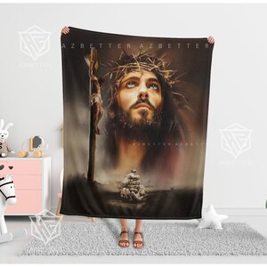 May include: A black fleece blanket with a painting of Jesus Christ on the cross. The painting is in a realistic style and features a close-up of Jesus' face. The background is a dark brown color.