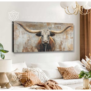 Könnte beinhalten: Ein rechteckiges Leinwandkunstwerk mit einem Longhorn-Bullen mit großen Hörnern. Der Bulle ist in Braun-, Weiß- und Grautönen vor einem strukturierten, neutralen Hintergrund gemalt. Das Kunstwerk wird über einem weißen Sofa mit dekorativen Kissen ausgestellt.