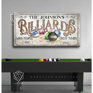 May include: A rectangular sign with the text "THE JOHNSON'S BILLIARDS" in brown script. The sign also includes the phrases "GOOD PEOPLE" and "GREAT TIMES" with the year "2022". Billiard balls are depicted on the sign. A black pool table is in the foreground.