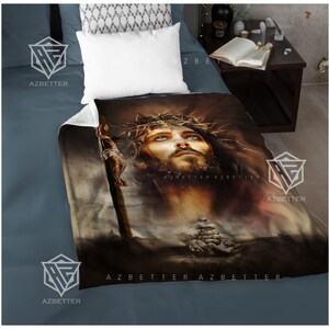May include: A brown and beige fleece blanket with a painting of Jesus Christ wearing a crown of thorns. The painting is in a realistic style and shows Jesus with his eyes closed and his head tilted back. The blanket has the text "AZBETTER" printed on it.