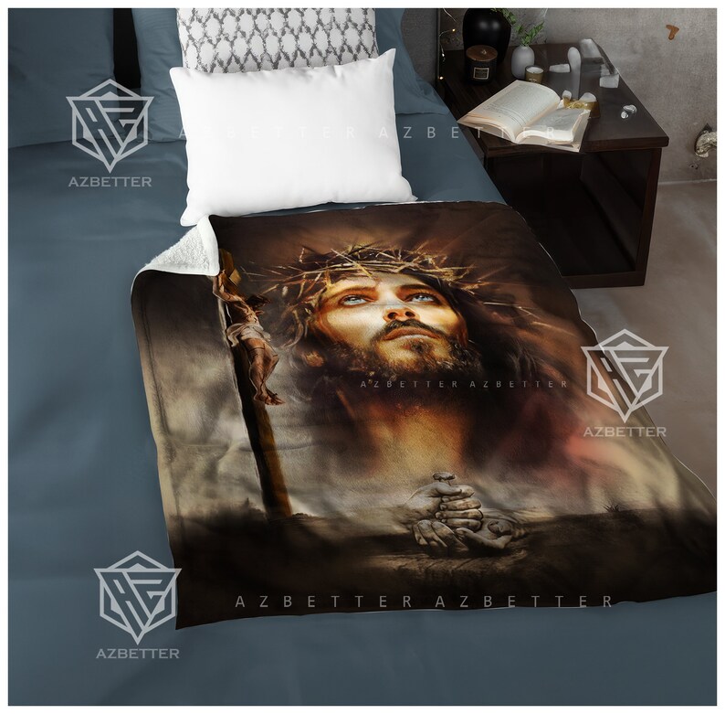 May include: A brown and beige fleece blanket with a painting of Jesus Christ wearing a crown of thorns. The painting is in a realistic style and shows Jesus with his eyes closed and his head tilted back. The blanket has the text "AZBETTER" printed on it.