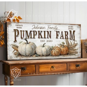 May include: A rectangular wooden sign with the words "Pumpkin Farm" in large, dark brown letters. The sign features illustrations of pumpkins and corn, with the text "Johnson Family" and "Est. 2020". The sign is displayed on a wooden table.