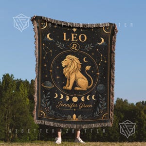 May include: A black woven throw blanket featuring a gold-colored lion illustration, the text LEO, the zodiac symbol, moon phases, stars, and planets. The name Jennifer Green is printed in gold script at the bottom, finished with a fringed edge.