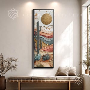 May include: A framed vertical canvas art piece depicting a desert landscape. The artwork features a textured gold sun, a tall cactus, and various desert plants in shades of green, blue, and brown. The background shows layered earth tones.
