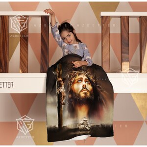 May include: A black and brown throw blanket with a graphic image of Jesus Christ on the cross. The blanket is draped over a wooden railing with a young girl sitting on it.