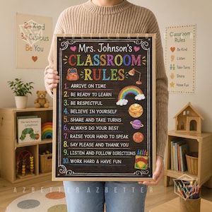 May include: A rectangular classroom rules sign with a black chalkboard background and a light wood frame. The text reads Mrs. Johnson's CLASSROOM RULES followed by a numbered list of ten rules, decorated with colorful illustrations of a backpack, rainbow, planets, and crayons.