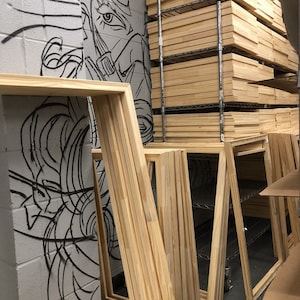 May include: A stack of wooden canvas stretcher bars in various sizes, leaning against a wall with a black and white line drawing of a face.