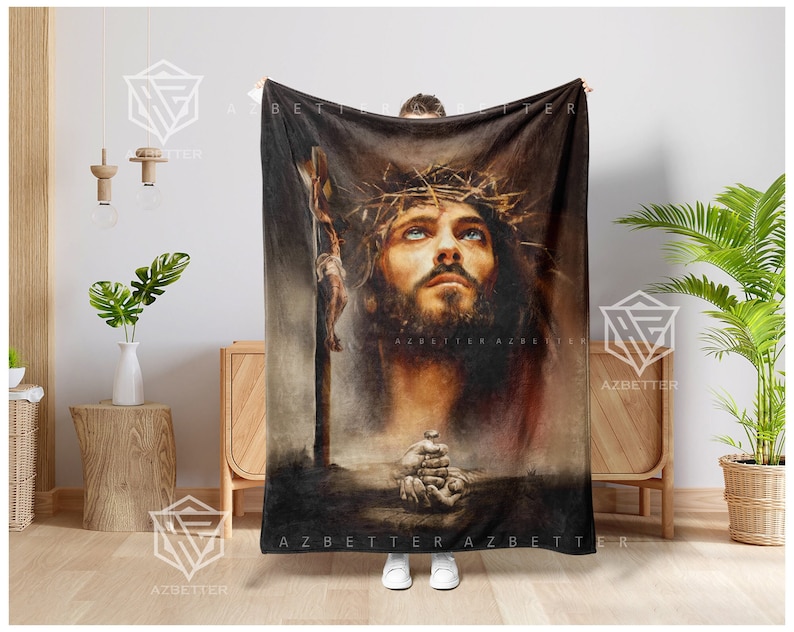 May include: A brown fleece throw blanket with a painting of Jesus Christ wearing a crown of thorns. The painting is in a realistic style and the background is a dark brown.