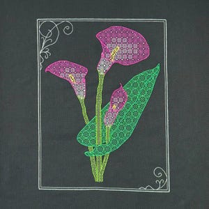 May include: Embroidered floral design featuring three calla lilies with pink and green patterned details. The lilies are set against a black background within a white rectangular frame with decorative corner elements. The design is a botanical theme.