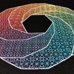 以下が含まれることがあります： 黒い布地に刺繍されたカラフルな幾何学模様。デザインは、中央に八角形のあるらせん状のパターンを特徴としています。