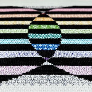 May include: A black and white cross-stitch pattern with a rainbow design in the center. The pattern features a variety of geometric shapes and designs.