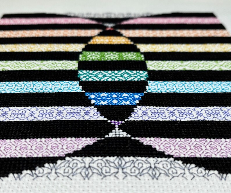 May include: A black and white cross-stitch pattern with a rainbow design in the center. The pattern features a variety of geometric shapes and designs.