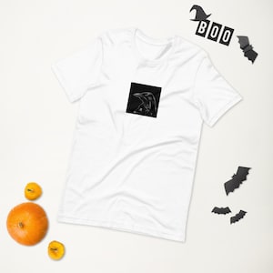 Könnte beinhalten: Weißes T-Shirt mit einem schwarz-weißen Bild eines Rabens auf der Vorderseite.