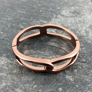 Puede incluir: Un brazalete de oro rosa con un diseño de doble bucle. El brazalete está hecho de metal y tiene un acabado pulido.