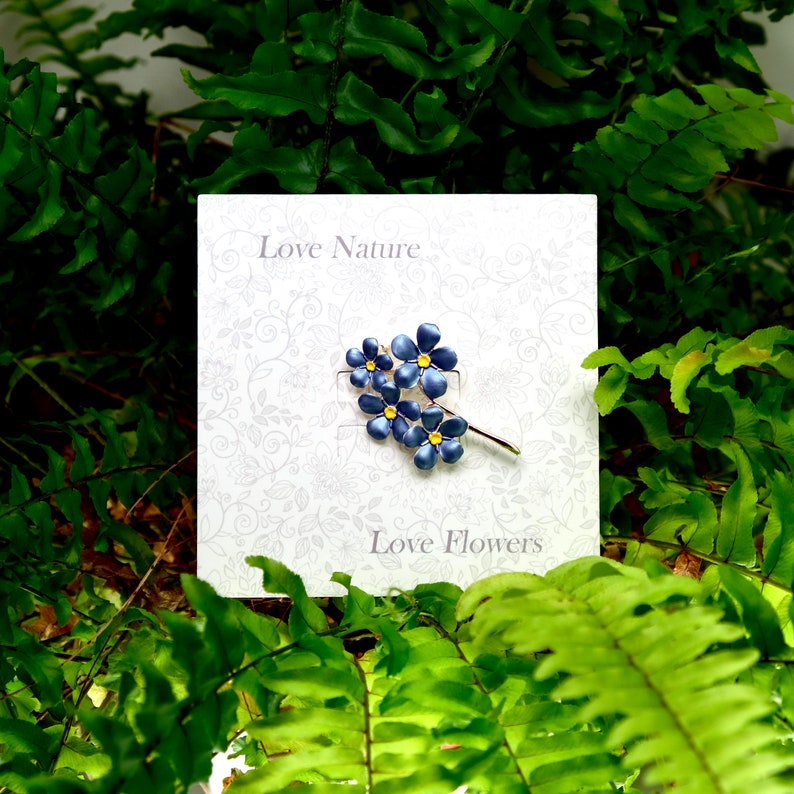 Forget me not blue flower brooch jewellery gift by ATLondonJewels, on a gift card, against a foliage background.