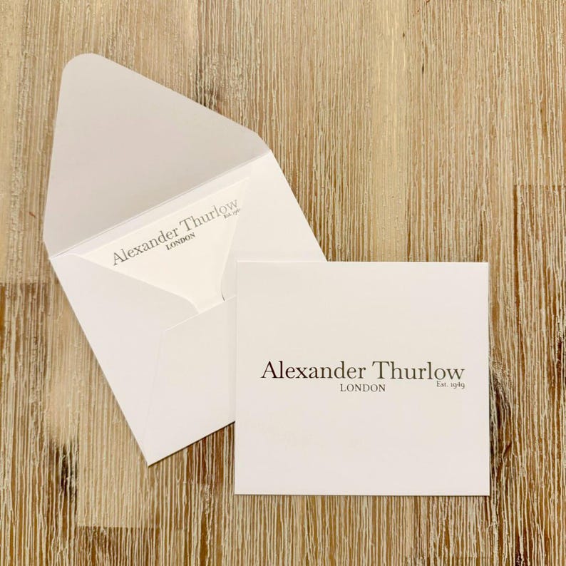 May include: White stationery set featuring a square card and an open envelope, both with the text "Alexander Thurlow LONDON Est. 1949" in dark brown. The set is displayed on a light brown wooden surface.