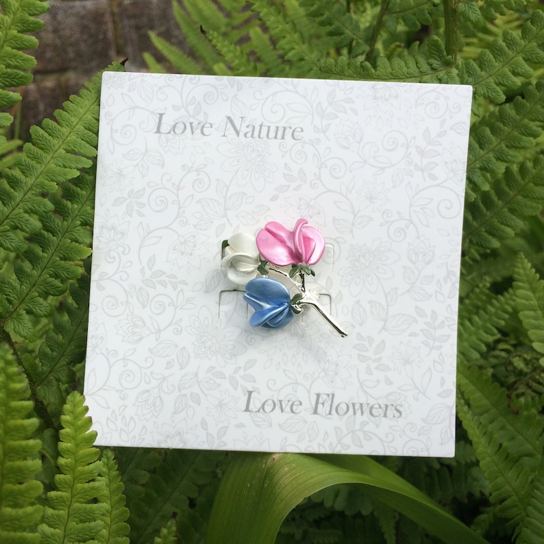 Sweet pea brooch jewellery gift with blue, white and pink flowers, by ATLondonJewels on a gift card against a foliage background.