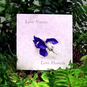 Iris brooch on display card, set amongst green foliage background