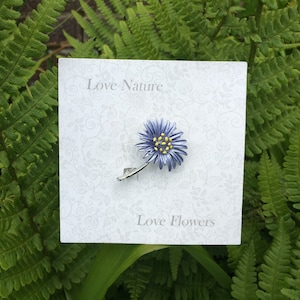 Aster blue flower brooch jewellery gift by ATLondonJewels, on a card against a foliage background.