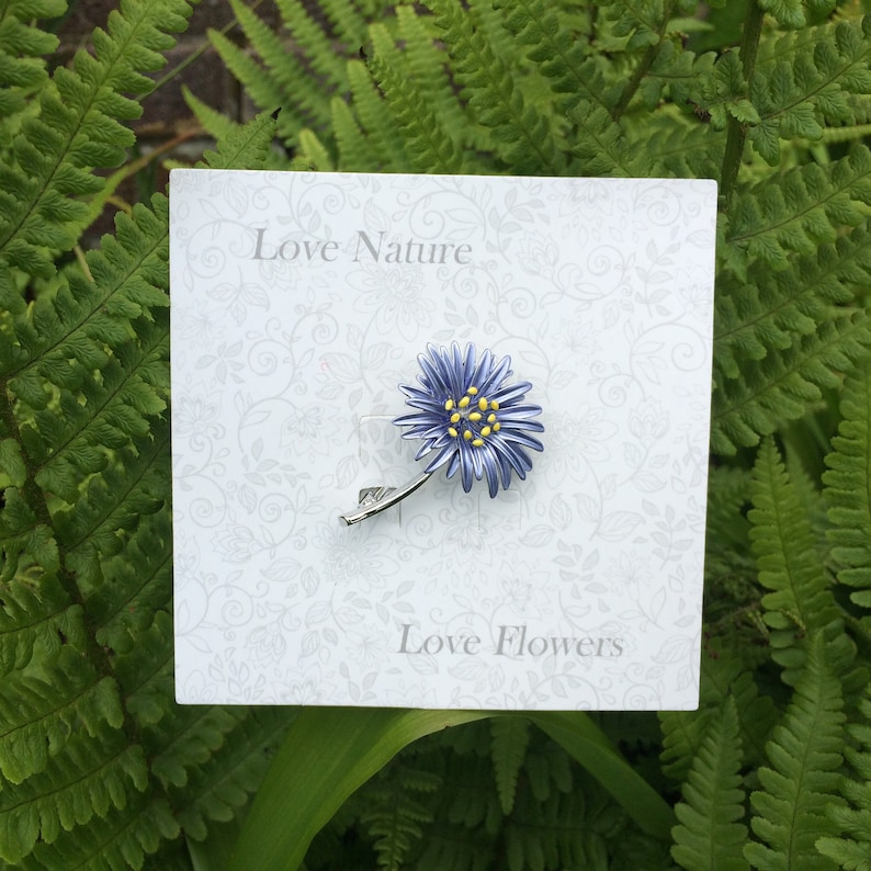 Aster blue flower brooch jewellery gift by ATLondonJewels, on a card against a foliage background.